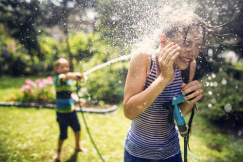 Little boy is splashing his sister with garden hose. on a sunny summer day. - KM Family Law