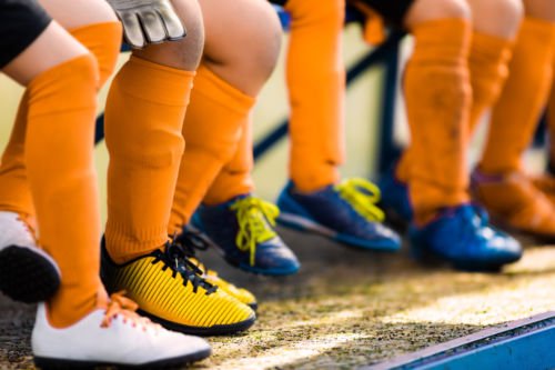 Youth athletes in soccer clothes sitting on a bench in a row. - KM Family Law